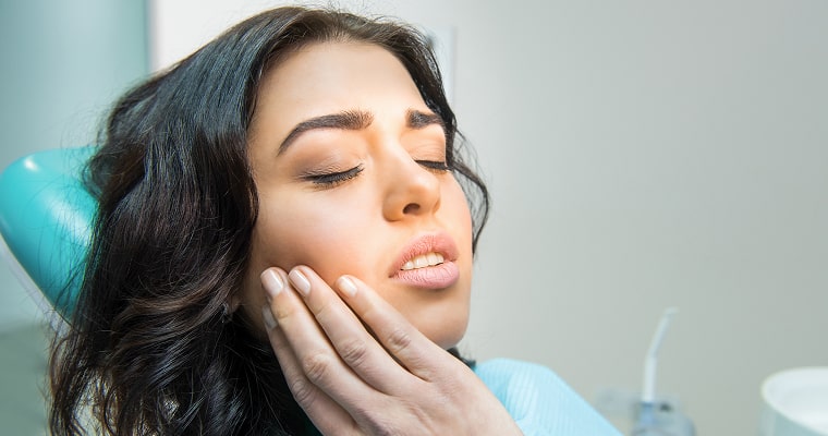 Woman in a dentist's chair holding her jaw in pain